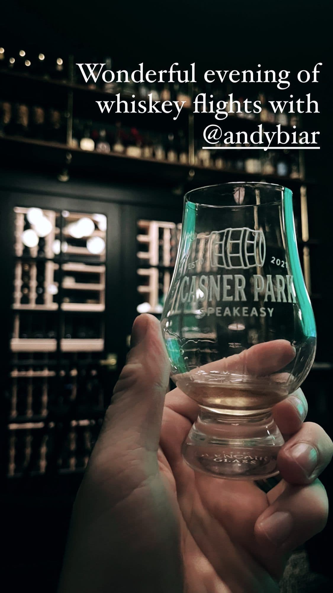 Custom Casner Park Speakeasy Glencairn glass held up with the bar behind