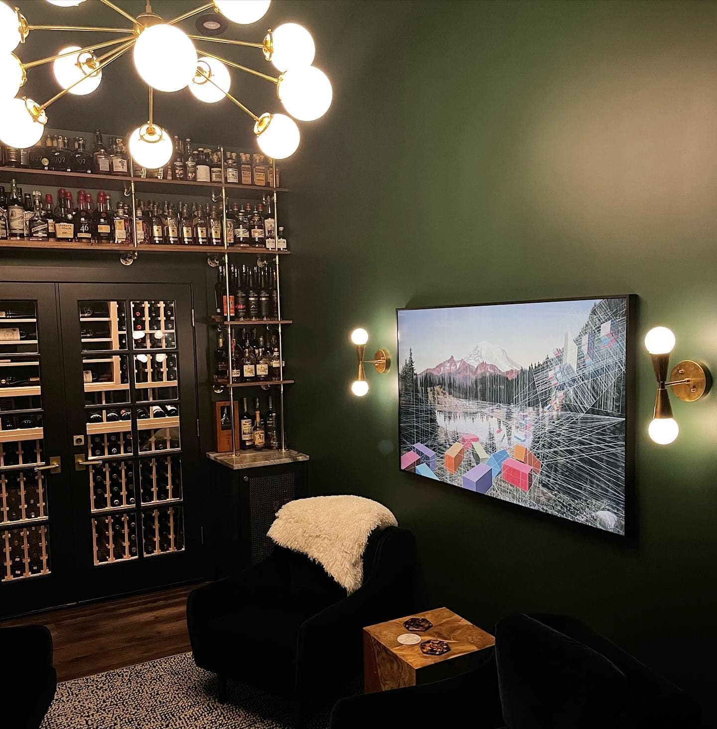 Frame TV showing art on the green wall, chandelier above, whiskey shelves behind