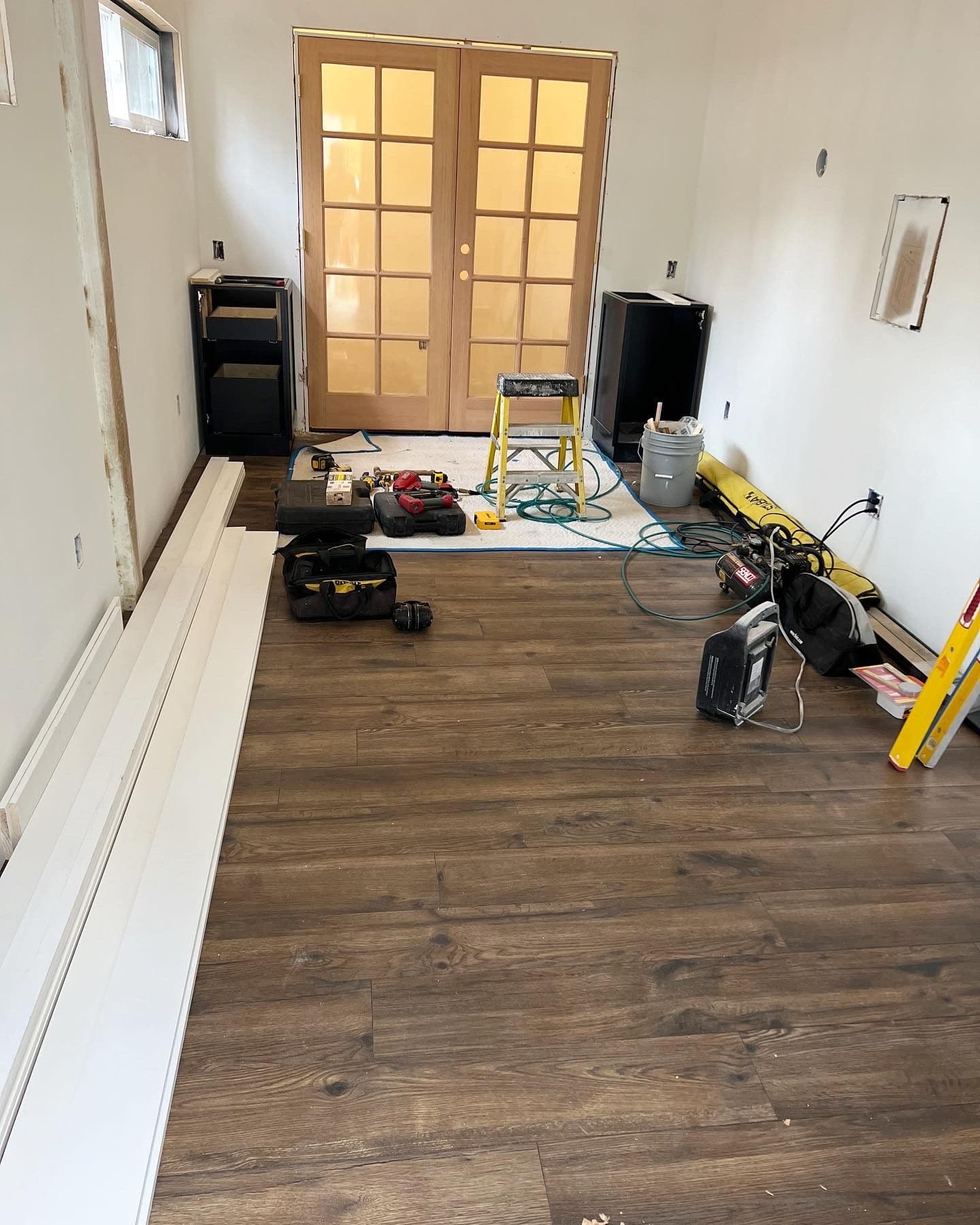 Dark hardwood flooring being installed with French doors visible