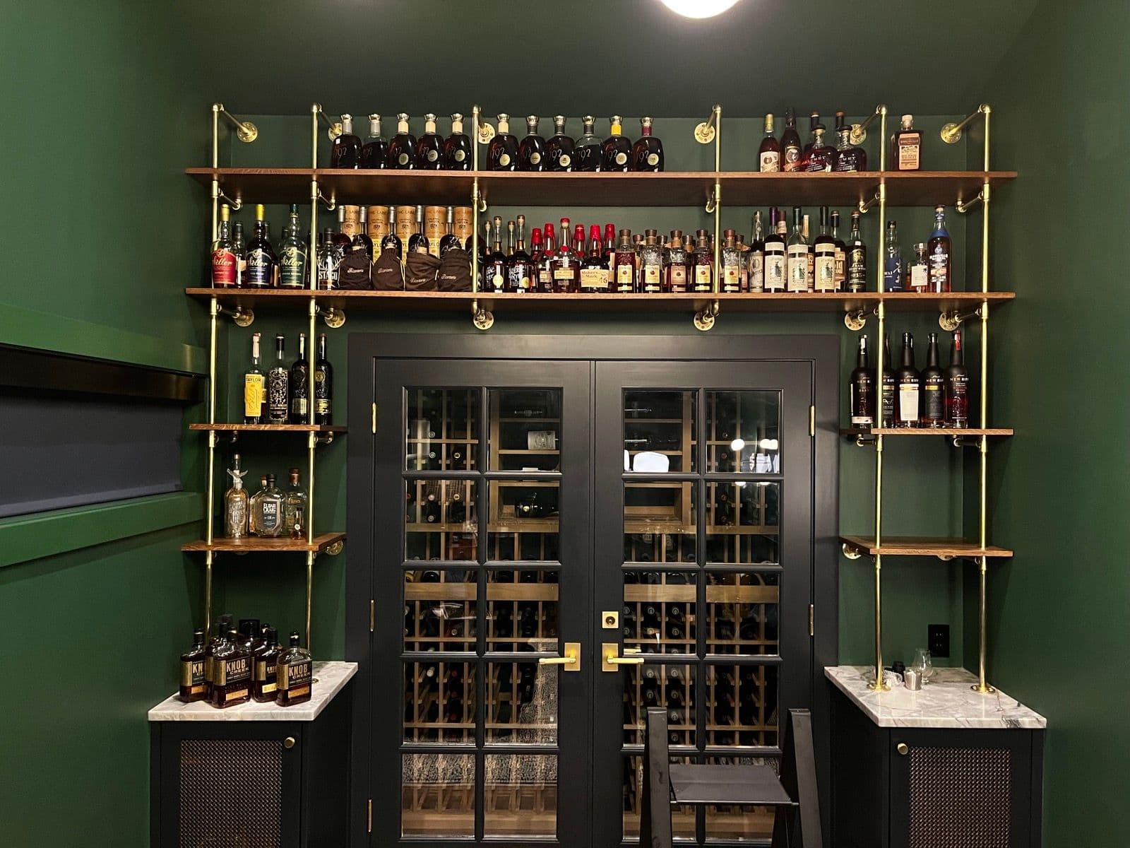 The finished bar wall — brass shelving lined with bottles